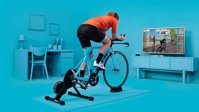 Ciclista con rodillo en habitación azul usando Zwift